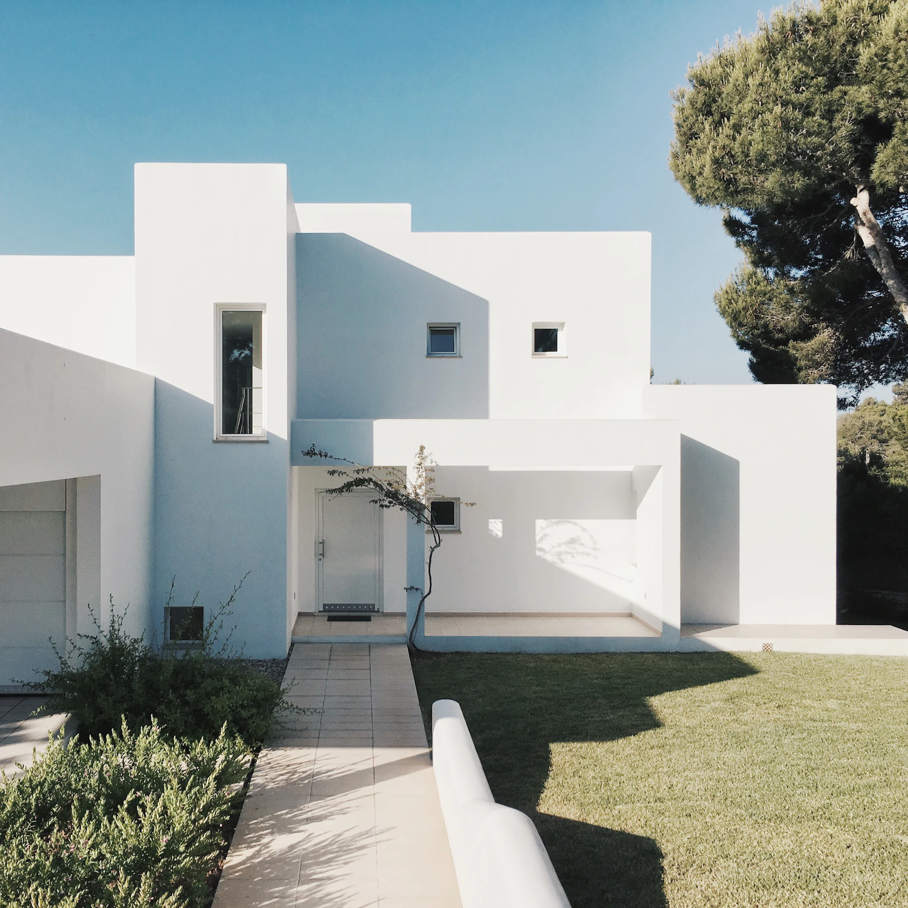 Placeholder photograph of a white sculptural residence with a lawn and pine tree